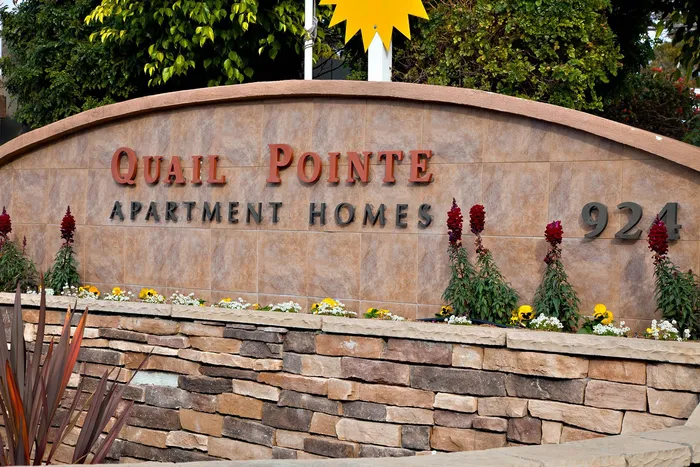 Stone monument sign for Quail Pointe Apartment Homes surrounded by colorful flowers.