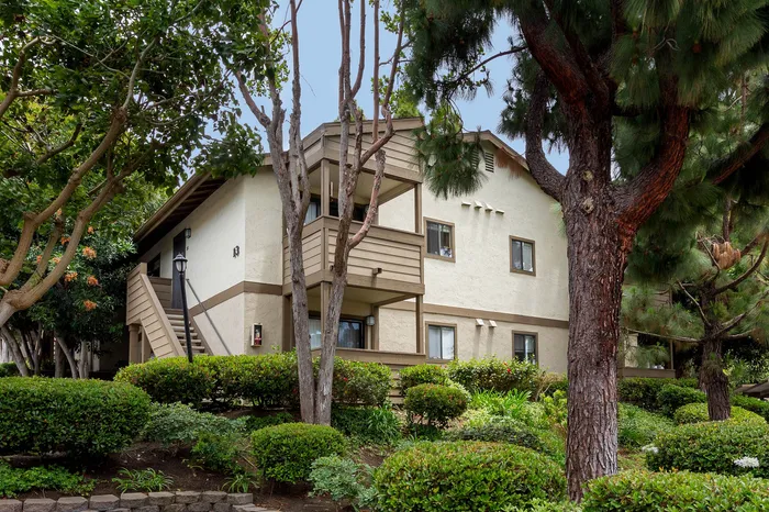 Exterior view of a two-story apartment building with private balconies and manicured hedges.