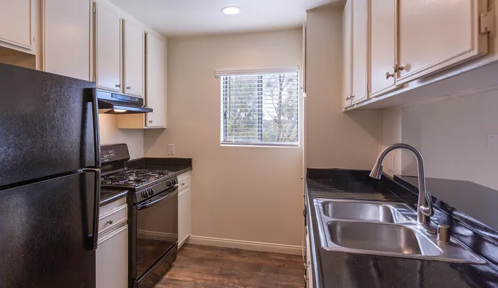 Modern kitchen featuring black appliances, wood-style cabinets, and a window for natural light.