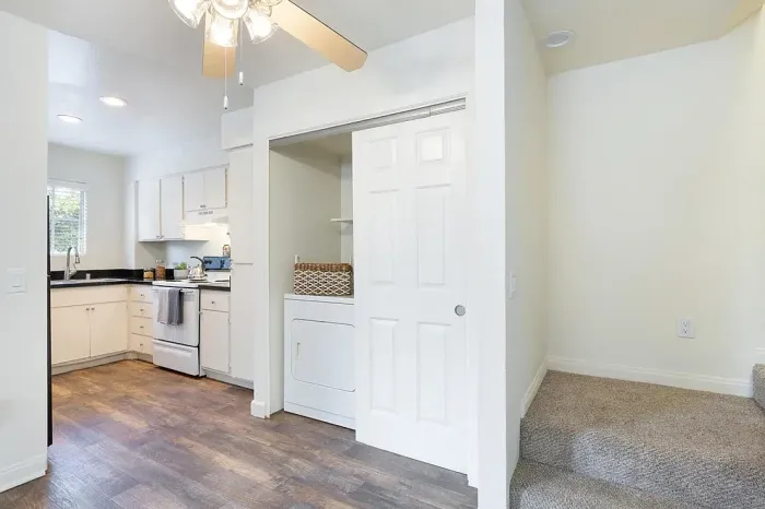 Interior view of an Elan Playa Mar apartment featuring wood-style flooring, a laundry closet with an in-home washer and dryer, and stairs leading to a second level.