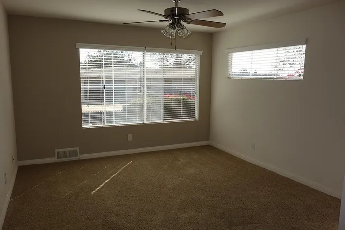 Bedroom featuring neutral-toned carpeting, a ceiling fan, and large windows.
