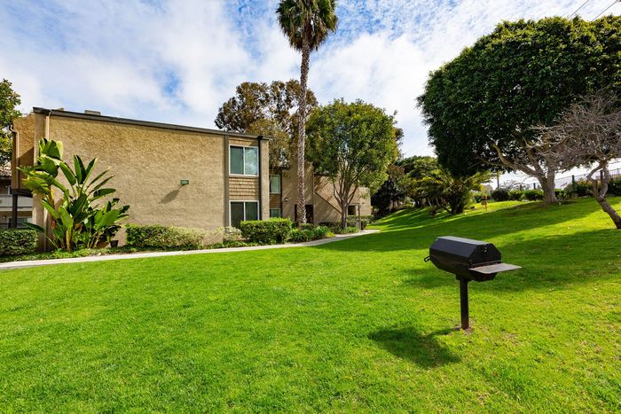 Open green space in the community featuring an outdoor barbecue area and mature trees.