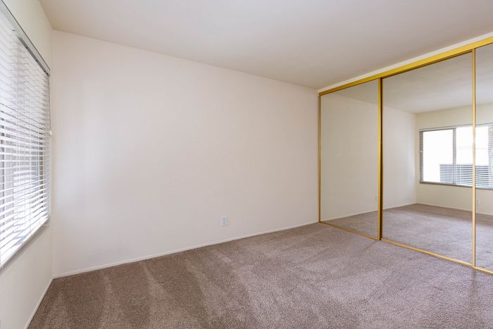 Bright bedroom featuring plush carpeting and large full-length mirror closet doors.