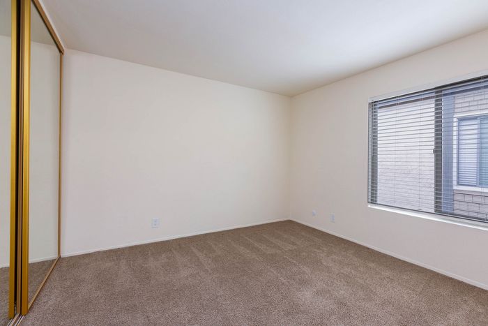 Bedroom interior showing a large window for natural light and ample closet space with full-length mirror doors.