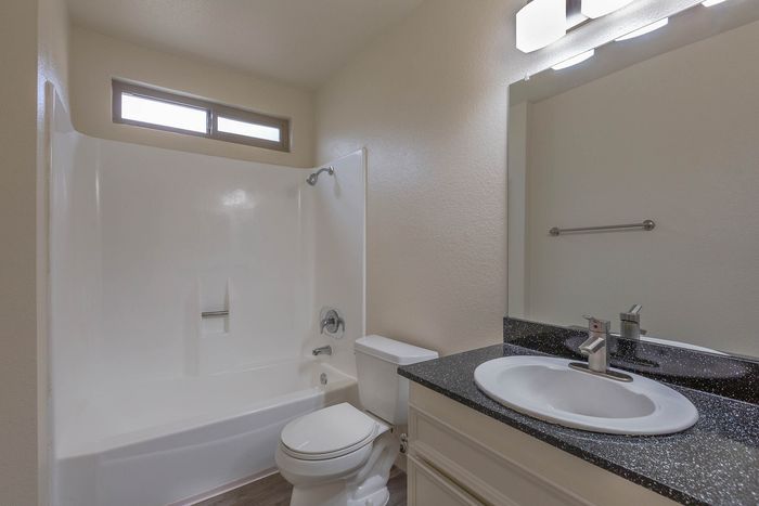 Clean, modern bathroom with white cabinetry, upgraded dark countertops, and a full bathtub with shower.