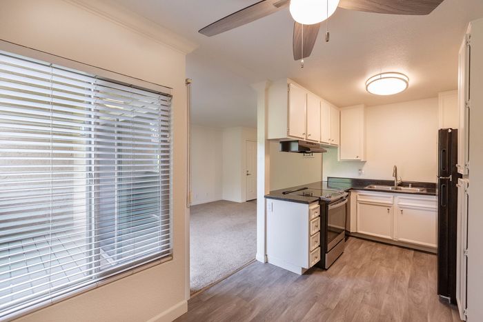 Modern kitchen area featuring wood-style flooring, white cabinets, and a large window providing natural light.