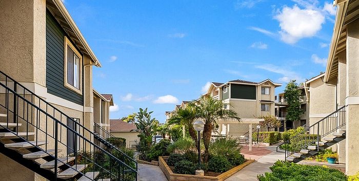 An outdoor view of the apartment community featuring landscaped walkways, stairs leading to private patios, and lush greenery.