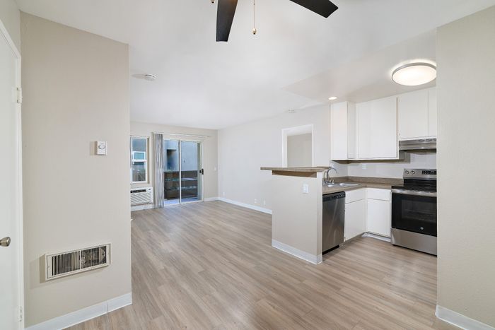 Open plan living and kitchen area with sink, dishwasher, oven, wooden floors, and ceiling fan