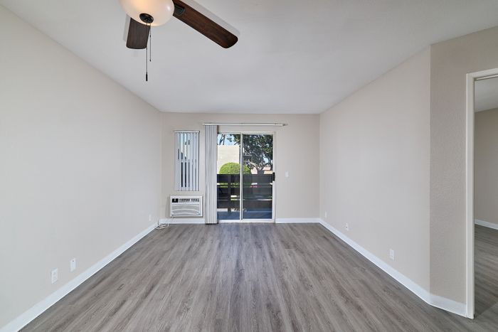 Living space with wooden floors, balcony, ceiling fan, and AC