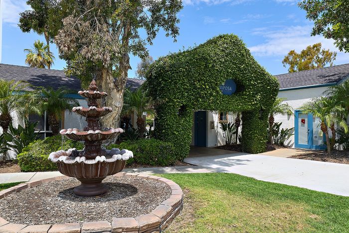Property entrance with fountain and greenery with blue skies.