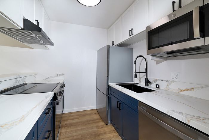 Kitchen in one bedroom at Melrose Canyon with navy cabinets, quartz countertops and wood floors, stainless appliances