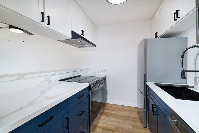 Kitchen in one bedroom at Melrose Canyon with navy cabinets, quartz countertops and wood floors, stainless appliances