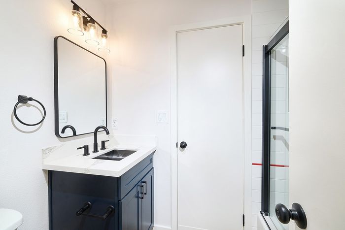 Bathroom at Melrose Canyon with navy cabinets, white counters, black accents and a shower/tub convo