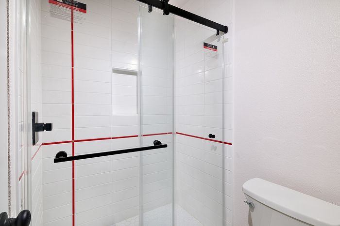 Shower in a two bedroom unit at Melrose Canyon with white tile and a red stripe with glass doors