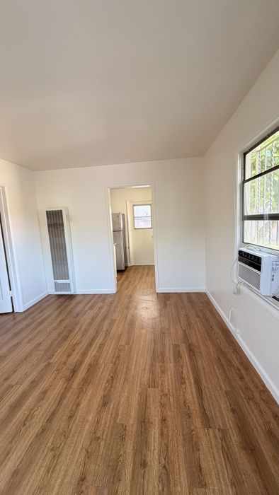 Living space with wooden floors, AC unit, fridge, and window.