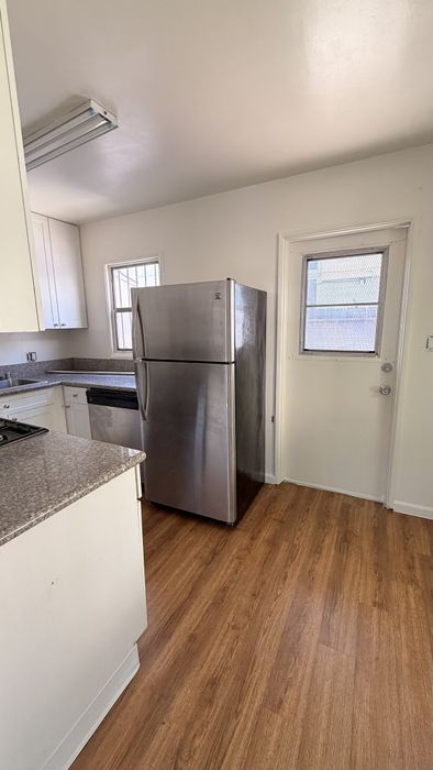 Kitchen with fridge, sink, window, counters, wooden floors, and cupboards.