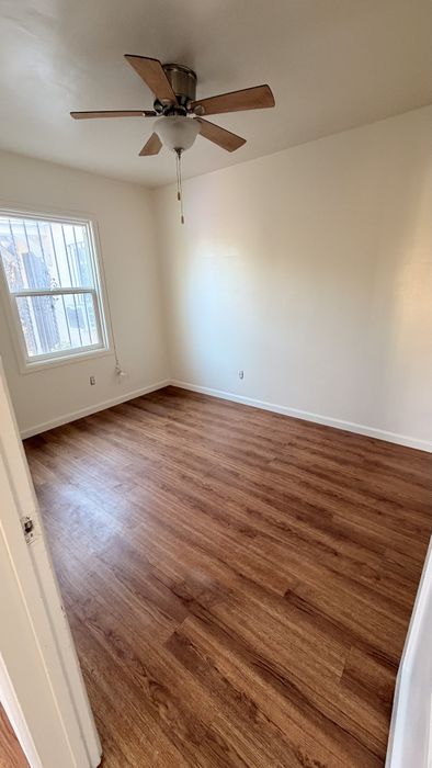 Bedroom with wooden floor, window, and plastered walls.