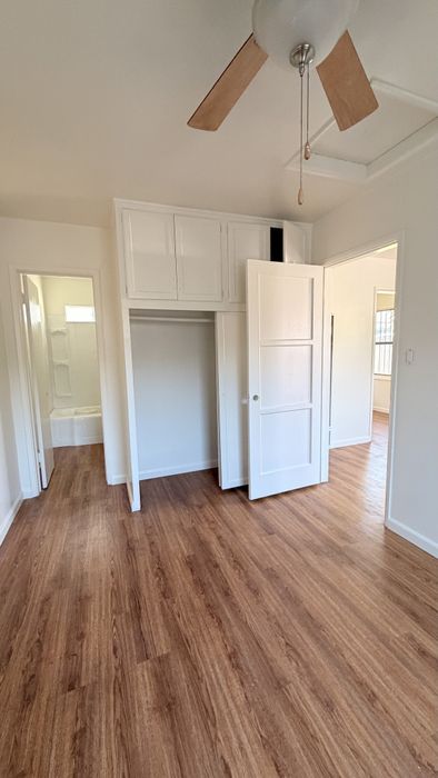 Bedroom with bathroom, closet, storage, wooden floors, and plastered walls.