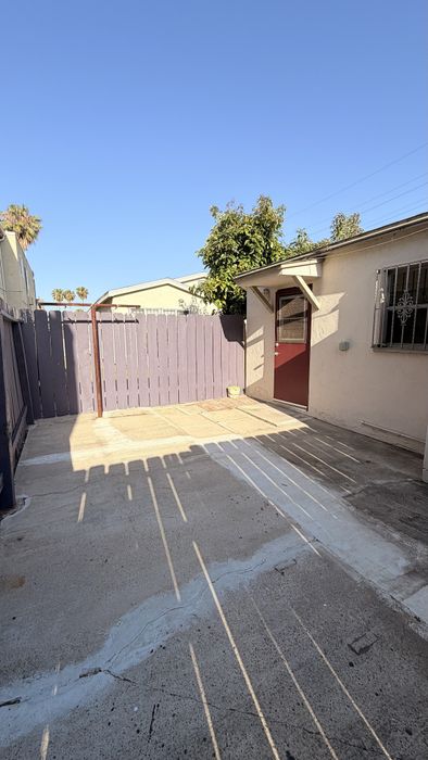 Patio area with fence, concrete, trees, and blue skies.