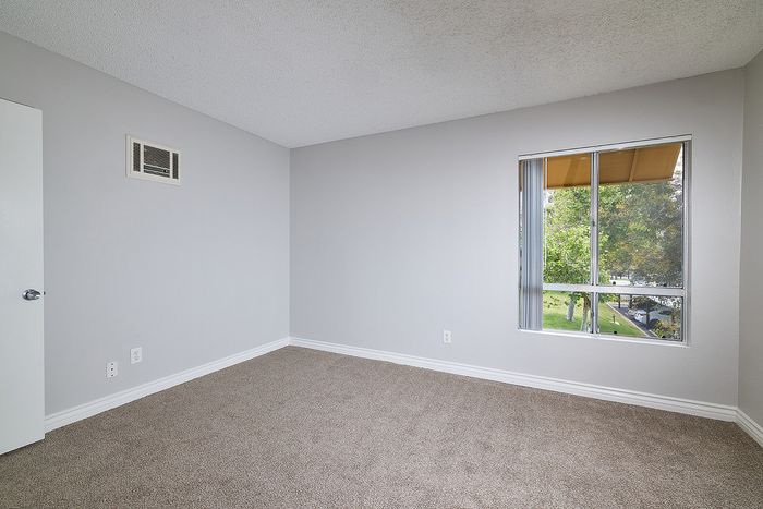Unstaged bedroom with carpet, window and AC.