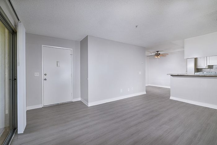 Unstaged living space with wooden floor, countertops, ceiling fan, patio, and kitchen.