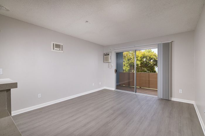 Unstaged living room with wooden floor, patio, and AC.