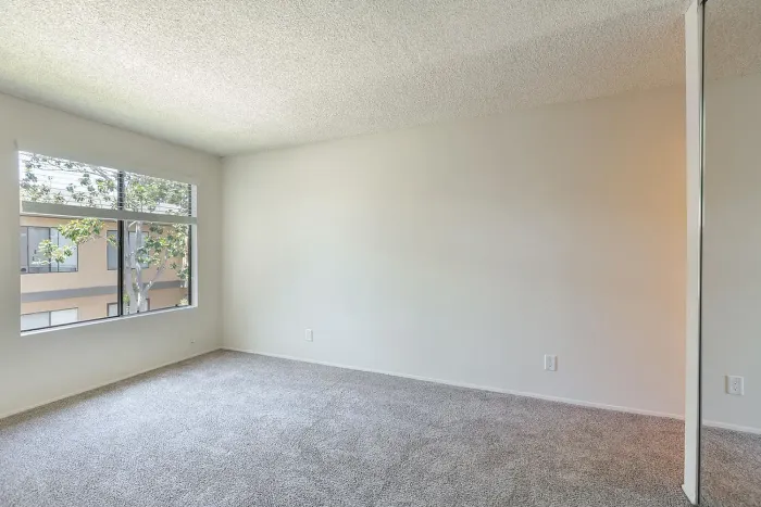 Sunlit bedroom with neutral walls and carpet at Elan - Scripps Terrace.