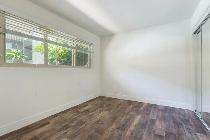 Bright bedroom with mirrored closet doors and wood-style floors at Elan - Baylofts