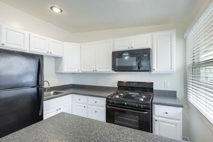 Modern kitchen featuring white cabinets and black appliances at Elan - beachcomber la jolla.