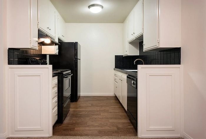 Galley kitchen featuring wood-style flooring and dark appliances at Elan - bella mer coronado.