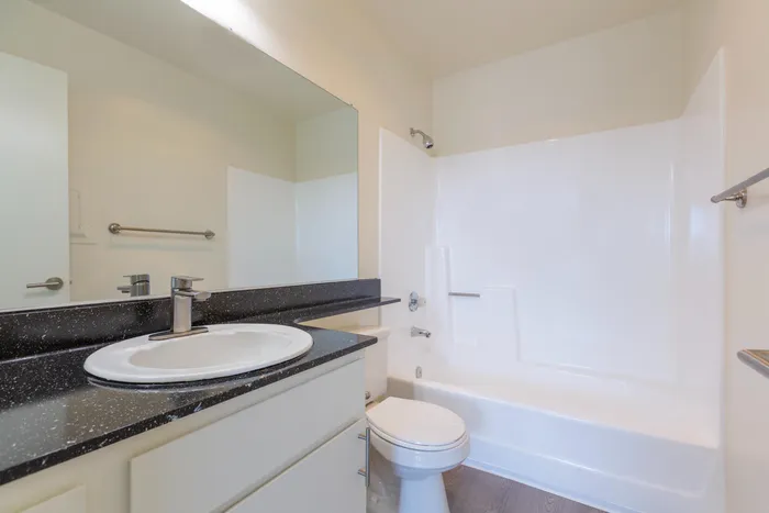 Modern bathroom featuring a large vanity mirror, dark countertop with an oval sink, and a shower-tub combination.