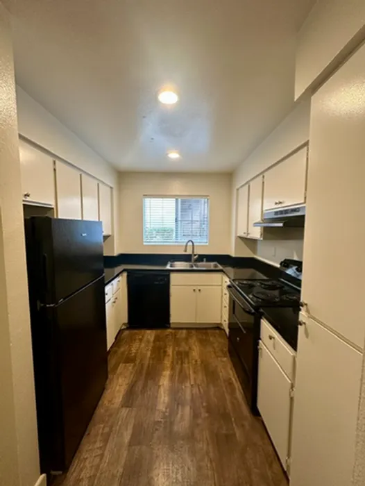 Fully equipped kitchen with white cabinetry, dark countertops, an electric range, dishwasher, and a window providing natural light.