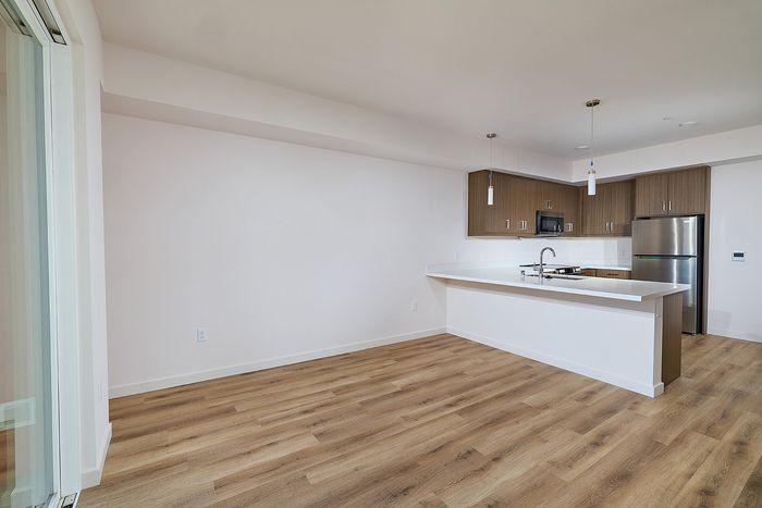 Dining area facing a modern kitchen with wood-finish cabinets and white quartz countertops at textur apartments.
