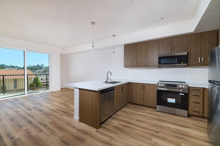Modern kitchen at textur with a quartz breakfast bar, stainless steel appliances, and adjacent balcony sliding door.