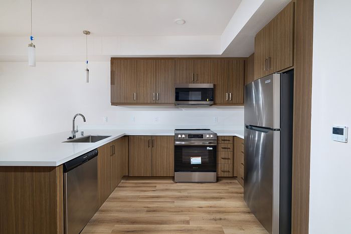 Textur apartment kitchen featuring stainless-steel appliances, flat-panel wood cabinets, and quartz countertops.