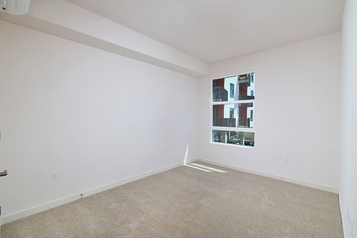 Carpeted bedroom at textur apartments in La Mesa, CA, featuring neutral paint and a large window with natural light.