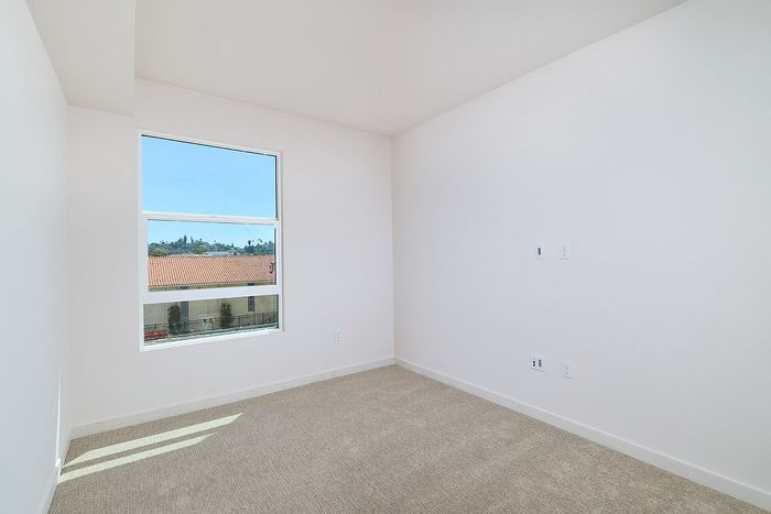 Bright bedroom at textur in La Mesa with beige carpeting, neutral walls, and a window overlooking neighborhood views.