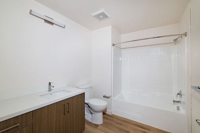 Modern bathroom at textur with a wood-finish vanity, white quartz countertop, toilet, and tiled tub-shower combo.