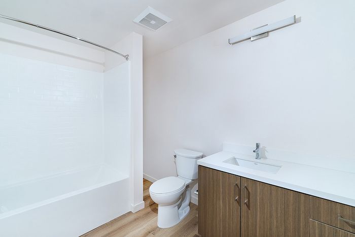 Clean bathroom at textur apartments with a wood-grain vanity, white countertops, toilet, and tiled tub-shower combo.