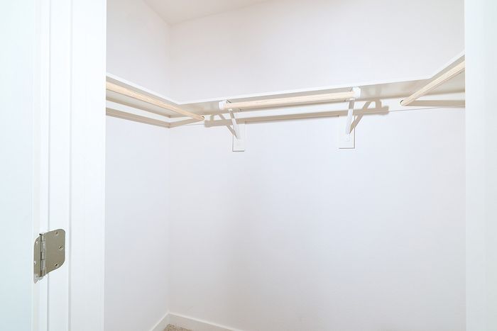 Spacious walk-in closet at textur apartments in La Mesa featuring white built-in shelving and wooden hanging rods.