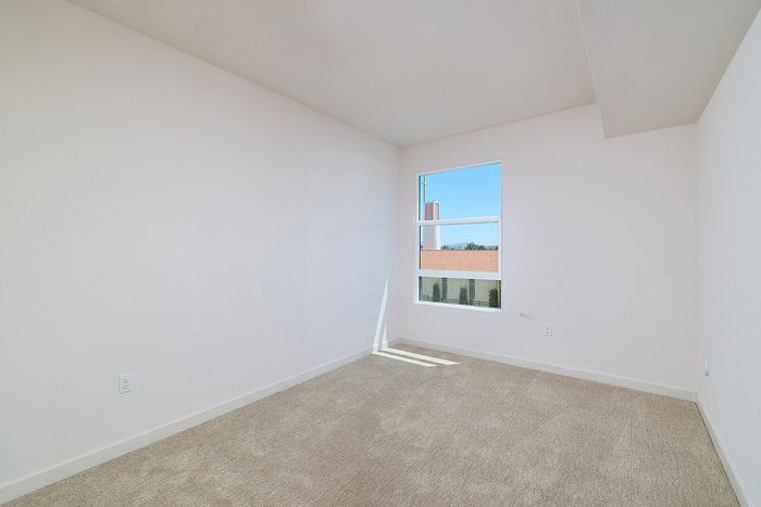 Carpeted bedroom at textur in La Mesa with a large window showing a church building and neighborhood roofs.