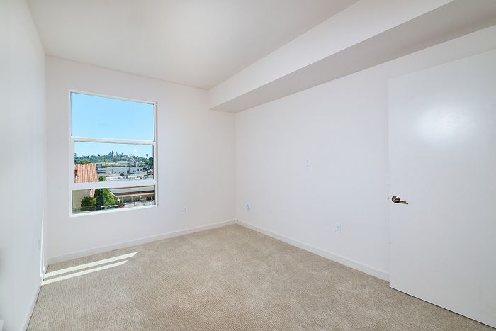Bright bedroom at textur apartments with beige carpeting, white walls, and a window showing La Mesa views.