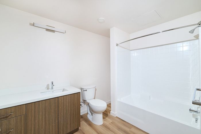 Modern apartment bathroom at textur with wood-finish vanity cabinet, white quartz countertops, and tub-shower.