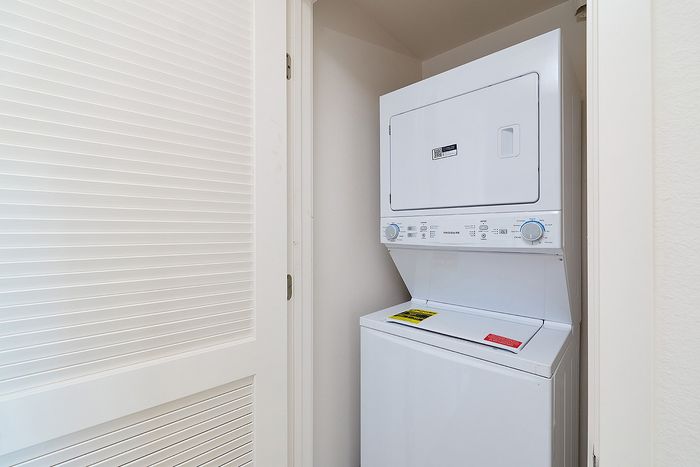 Utility laundry closet at textur apartments with stacked white washer and dryer behind a louvered white door.