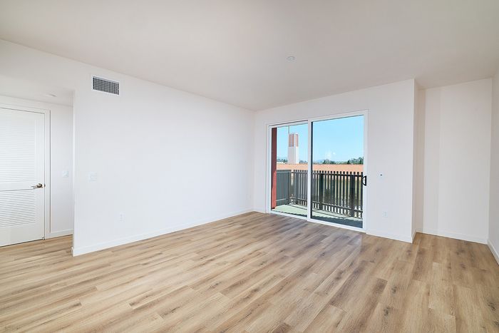 Light-filled living area in a textur La Mesa apartment with wood-style floors and a sliding glass balcony door.