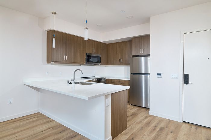 Modern kitchen at textur apartments with brown wood-grain cabinets, white countertops, and stainless steel appliances.