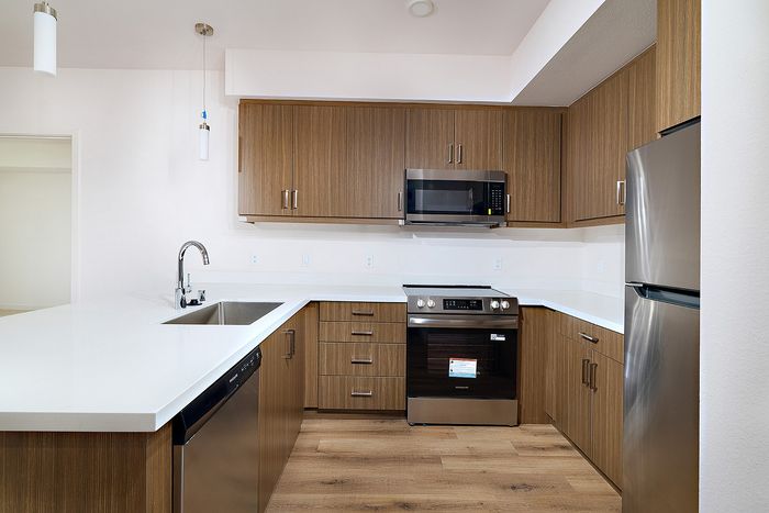 L-shaped kitchen at textur with stainless steel refrigerator, stove, microwave, dishwasher, and wood cabinets.