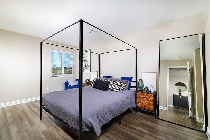Apartment bedroom with black canopy bed frame and floor mirror at The Warwick Apartment Homes.