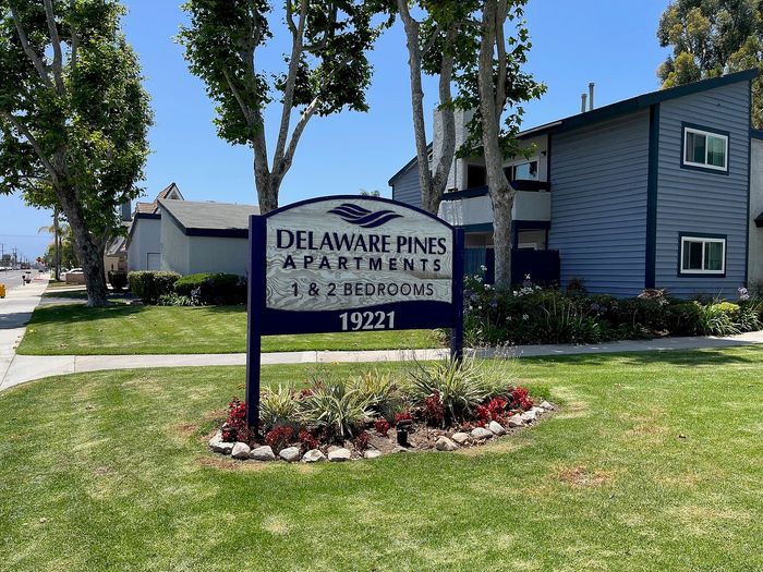 Delaware Pines Apartments monument sign with red flowers on a landscaped lawn in Huntington Beach.