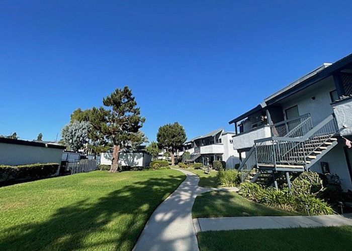 Shaded concrete pathway running alongside landscaped lawns and apartment building exteriors.